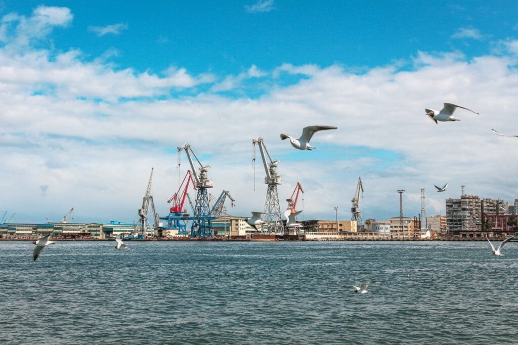 HFZA vs JAFZA manufacturing and logistics free zone comparison UAE 2026 — industrial port with cranes